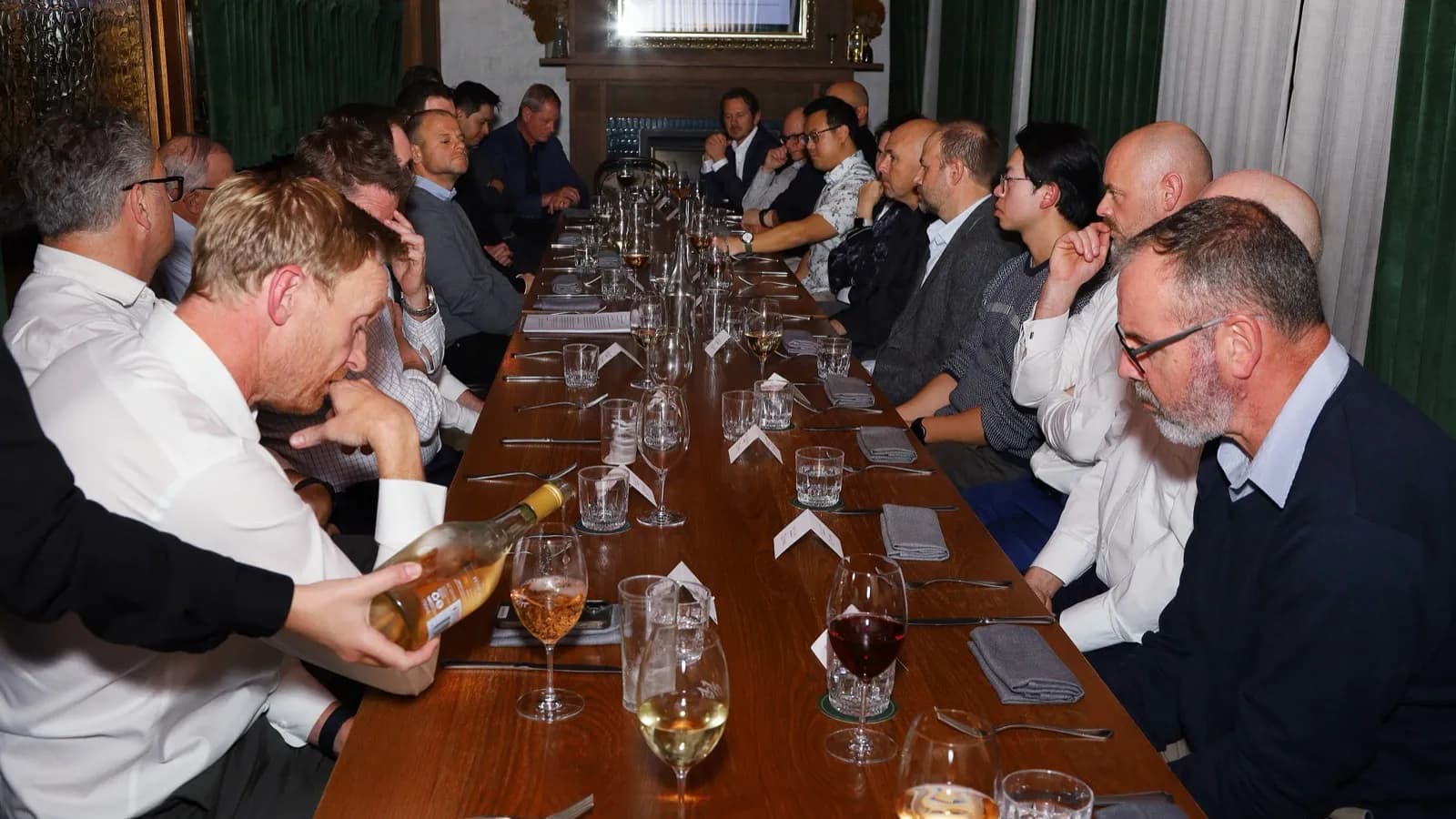 Guests seated along a long timber table in a private dining room, listening during the Construction Executives Dinner