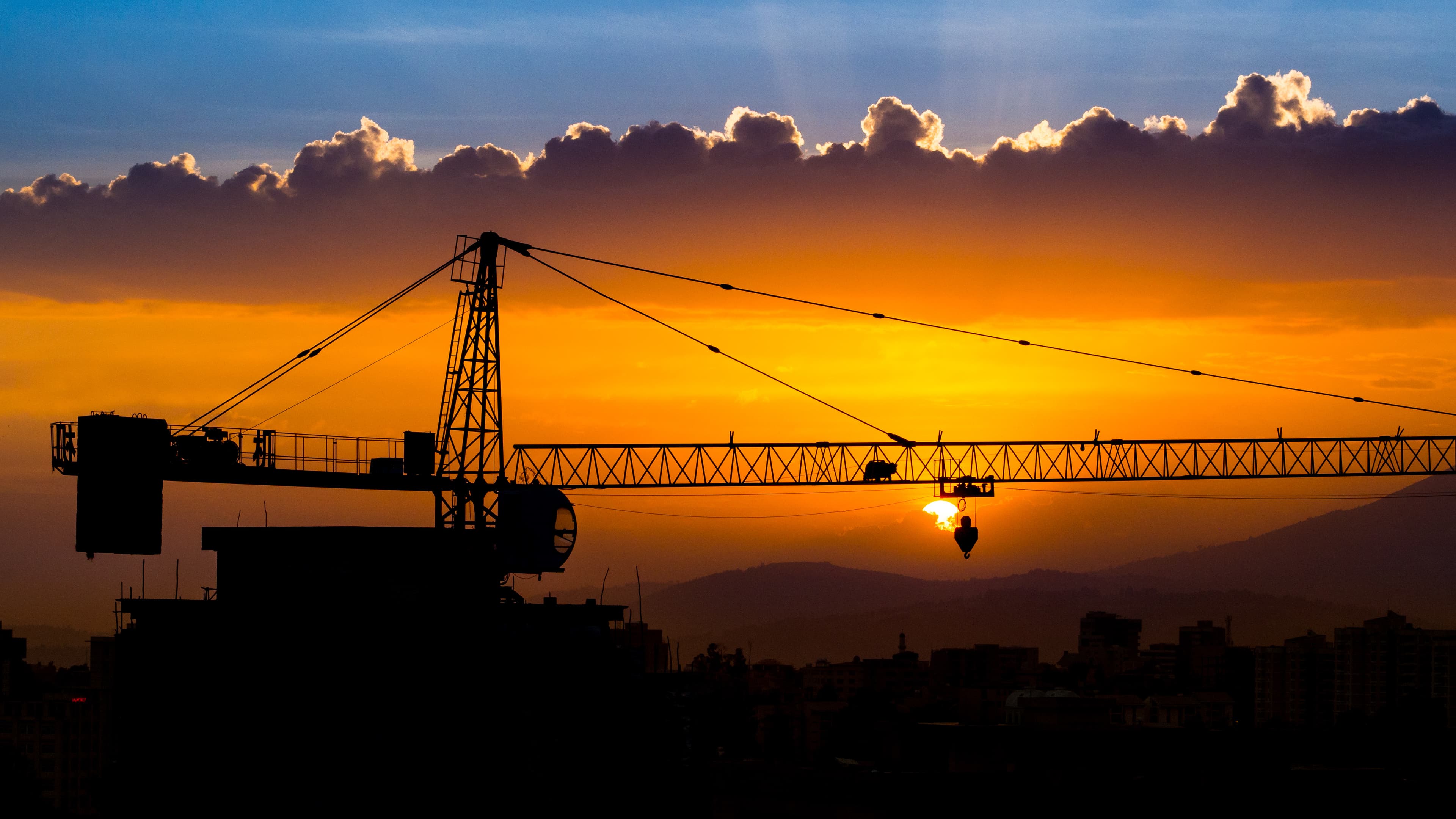 A tower crane lifting into a golden sunset over a rising city skyline